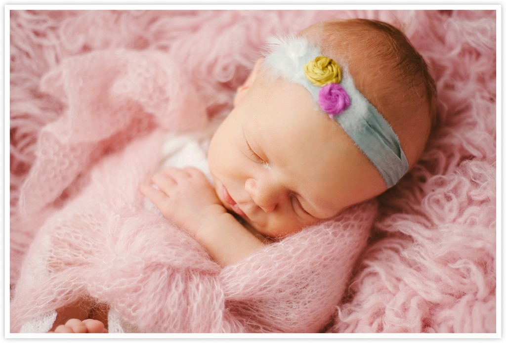newborn girl with headband and pink wrap on a pink rug
