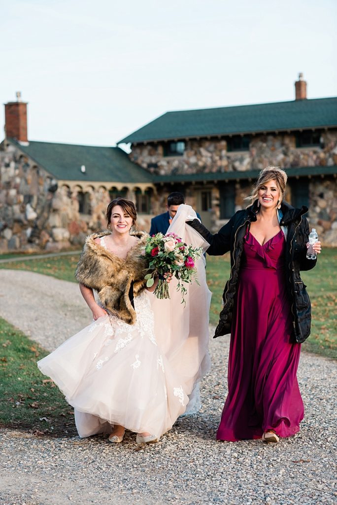 A bride and her bridesmaid walk away from the farmhouse at Stone House Farm, a Michigan barn wedding venue, by Allie & Co. Photography, Michigan wedding photographers