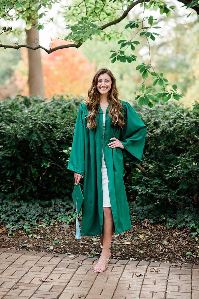 Ideas and locations for a Michigan State University fall senior photo session on north campus by Allie Siarto Photography, East Lansing Photographers. A photo of an MSU senior standing on bricks with her cap and gown and fall colors in the background.