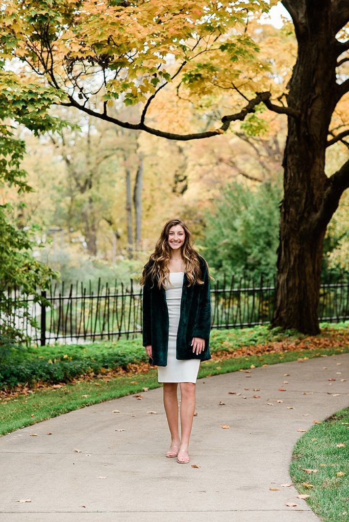 Ideas and locations for a Michigan State University fall senior photo session on north campus by Allie Siarto Photography, East Lansing Photographers. A photo of an MSU senior walking down the sidewalk with fall colors behind her.