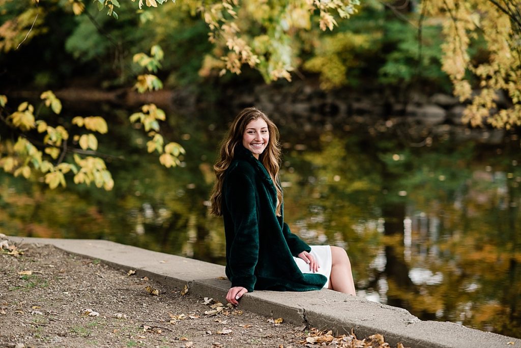 Ideas and locations for a Michigan State University fall senior photo session on north campus by Allie Siarto Photography, East Lansing Photographers. A photo of an MSU senior sitting by the Red Cedar river in the fall.