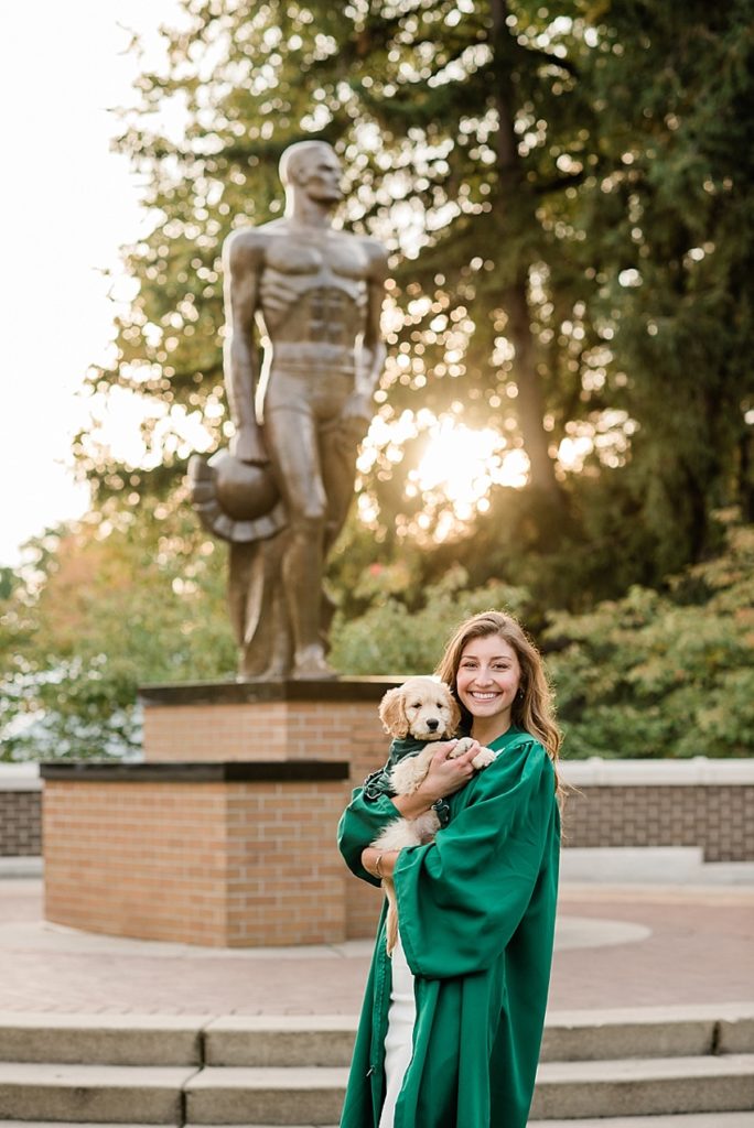 Ideas and locations for a Michigan State University fall senior photo session on north campus by Allie Siarto Photography, East Lansing Photographers. A photo of an MSU senior holding her puppy in front of Sparty at sunset.