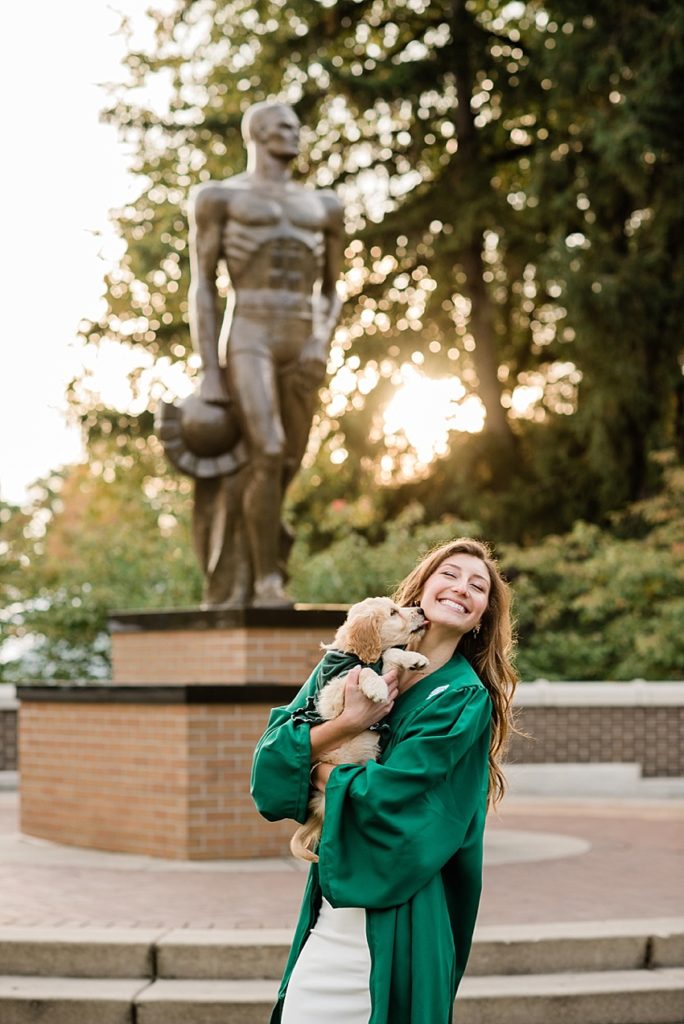 Ideas and locations for a Michigan State University fall senior photo session on north campus by Allie Siarto Photography, East Lansing Photographers. A photo of an MSU senior holding her dog in front of the Sparty Statue.