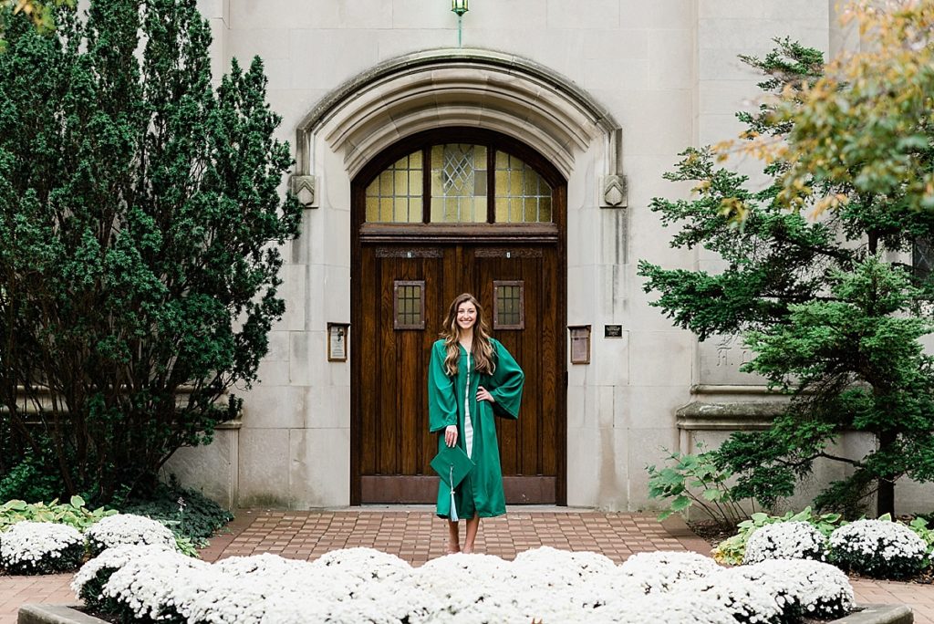 Ideas and locations for a Michigan State University fall senior photo session on north campus by Allie Siarto Photography, East Lansing Photographers. A photo of an MSU senior standing in front of the doors of Beaumont Tower with white flowers around her.