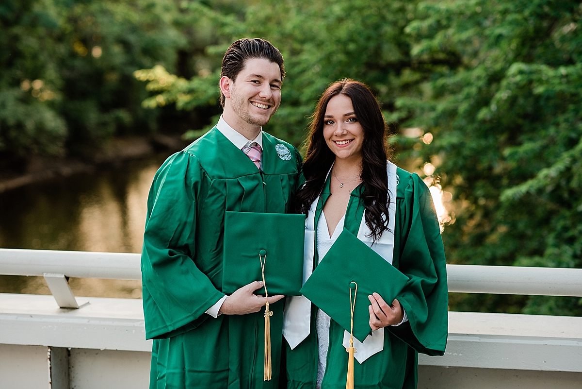 Michigan State Senior Pictures with a couple in caps and gowns on MSU's campus on the bridge by the library and Spartan Stadium overlooking the Red Cedar River, by Allie Siarto & Co. Photography, MSU graduation photographers