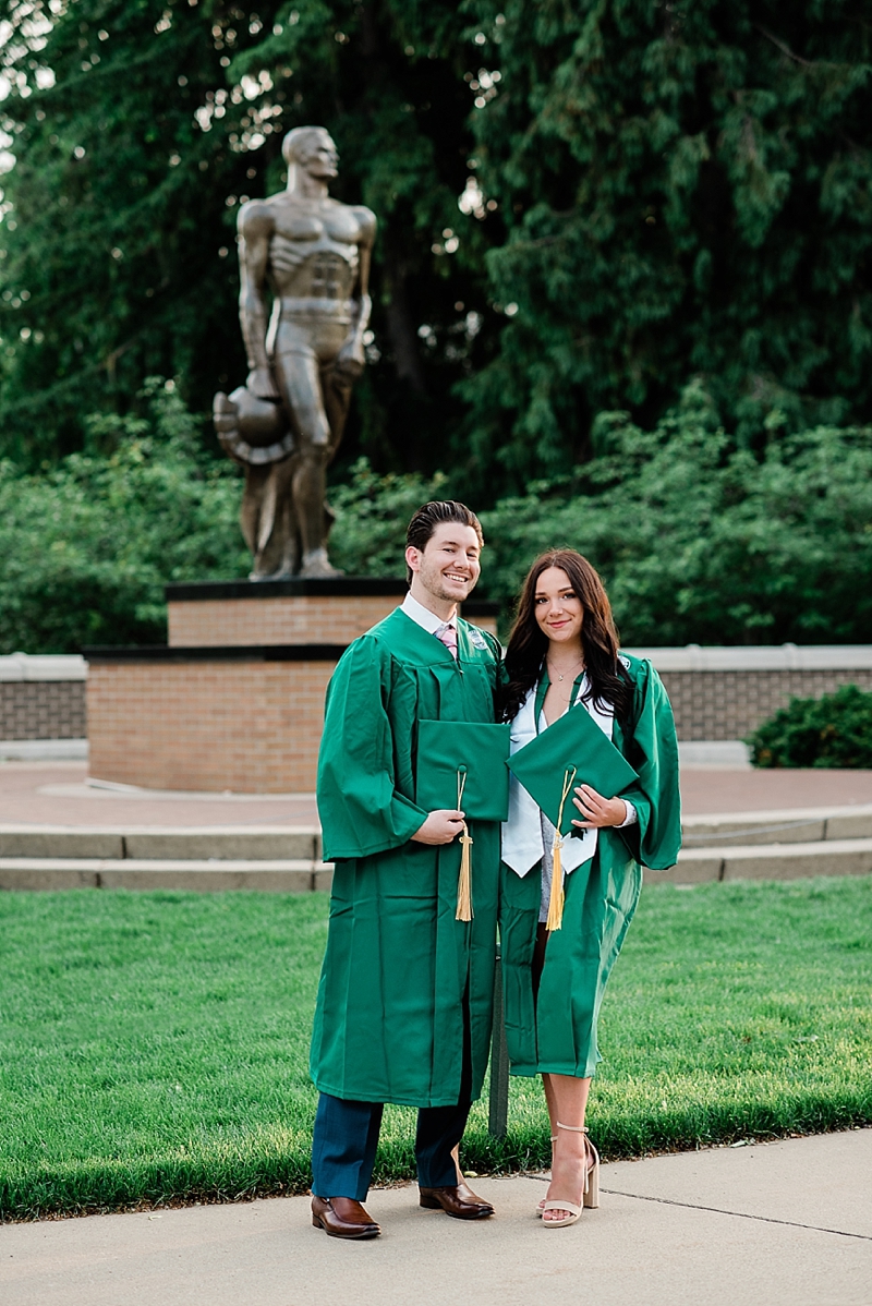 Michigan State Senior Pictures with a couple in a cap and gown on MSU's campus in front of the Sparty statue, by Allie Siarto & Co. Photography, MSU graduation photographers
