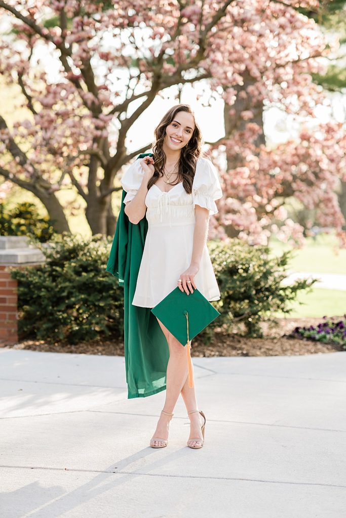 Michigan State University senior photo ideas with roommates on campus in white dresses and cap and gown over the shoulder with a magnolia tree in the background, by Allie Siarto & Co, senior photographers in East Lansing, Michigan