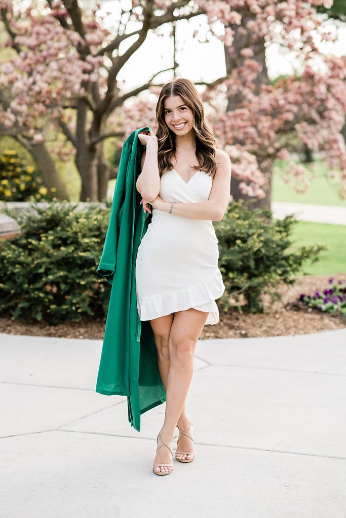 Michigan State University senior photo ideas with roommates on campus in white dresses and cap and gown over the shoulder with a magnolia tree in the background, by Allie Siarto & Co, senior photographers in East Lansing, Michigan