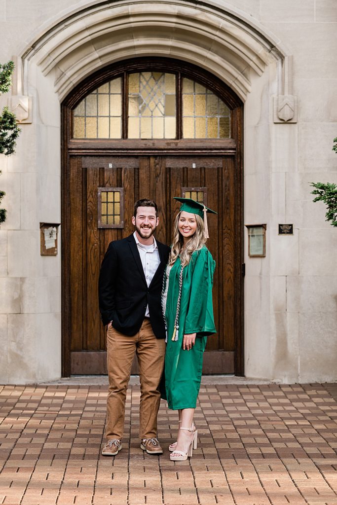 Michigan State University senior photography ideas with a couple on campus in white dresses and cap and gown in front of the door at Beaumont Tower, by Allie Siarto & Co, senior photographers in East Lansing, Michigan