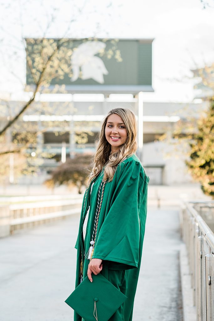 Michigan State University senior photography ideas with roommates on campus in white dresses and cap and gown on the bridge behind the library with the Spartan Stadium Sparty head in the background, by Allie Siarto & Co, senior photographers in East Lansing, Michigan