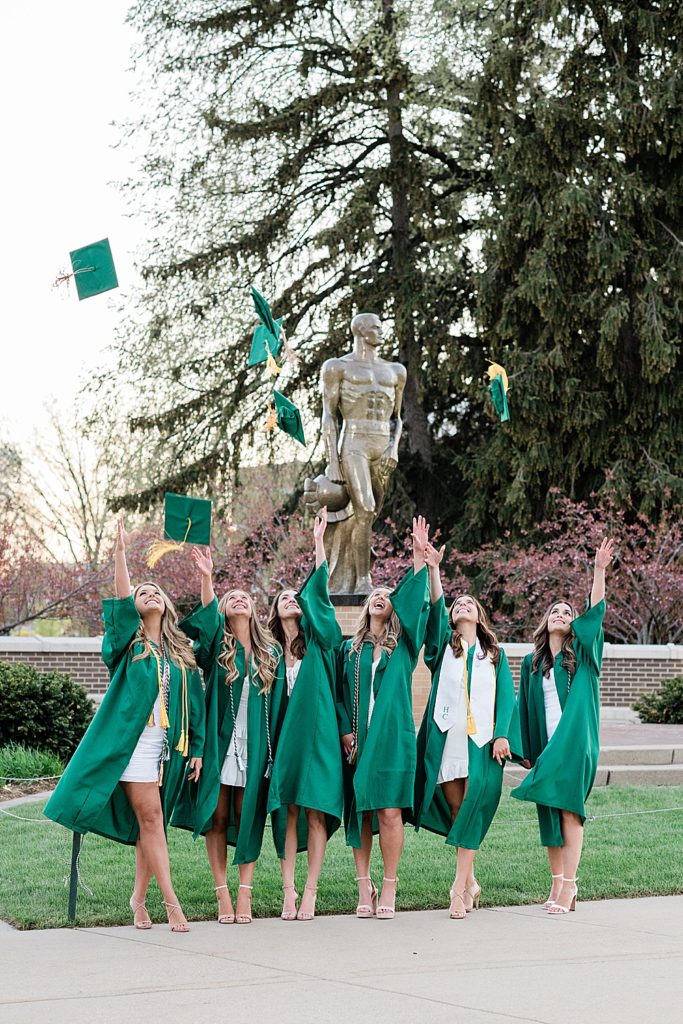 Michigan State University senior photography ideas with roommates on campus in white dresses and cap and gown throwing caps in the air in front of Sparty, by Allie Siarto & Co, senior photographers in East Lansing, Michigan