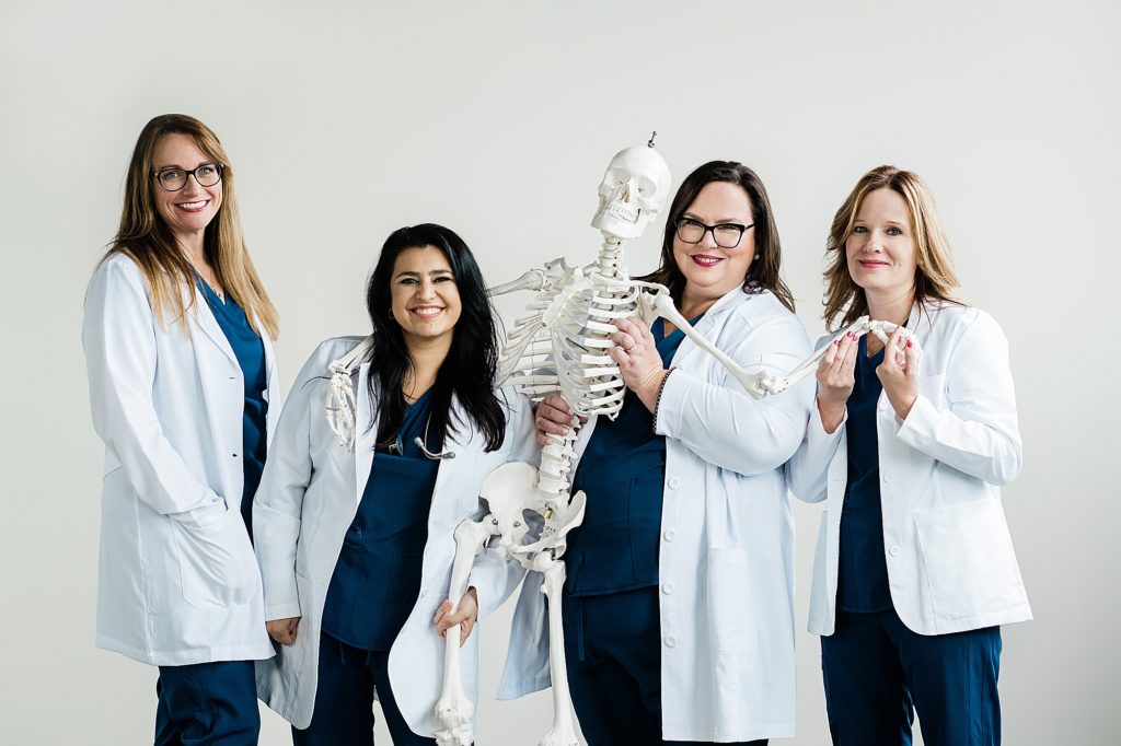 Studio branding headshots with four nurses with a skeleton on a white backdrop by Allie & Co. Photography in Lansing, Michigan