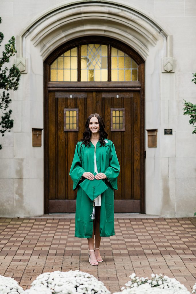 MSU graduation pictures on north campus in the fall with a white dress, holding a cap, and wearing a grad gown with the Beaumont Tower door in the background by Allie & Co. Photography, East Lansing photographers