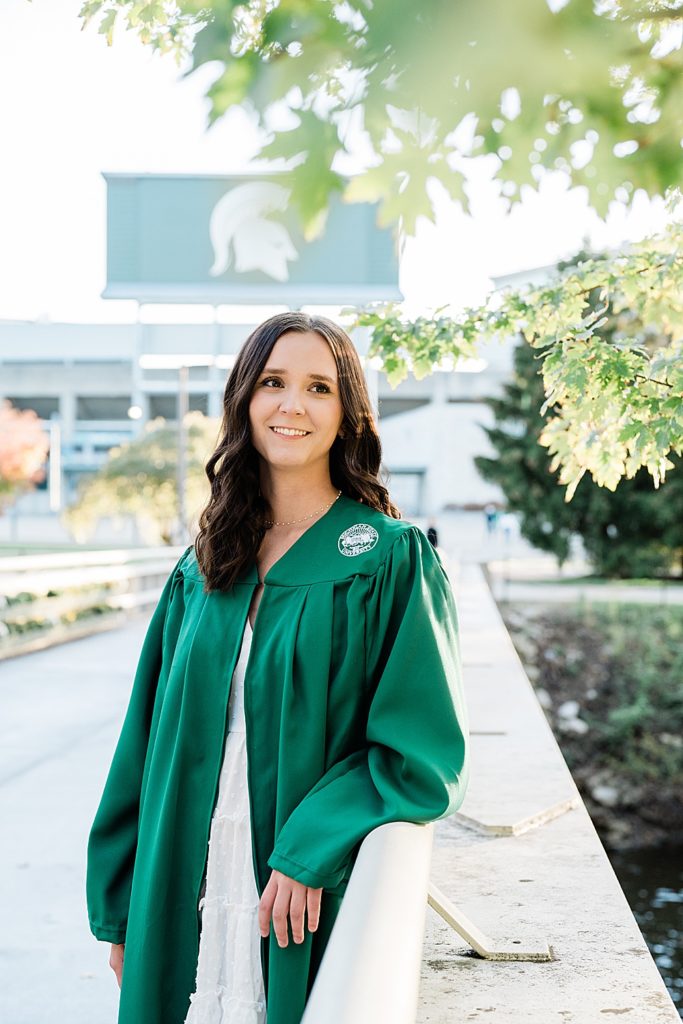 Michigan State graduation pictures on north campus in the fall with a white dress and grad gown with Spartan Stadium in the background by Allie & Co. Photography, East Lansing photographers