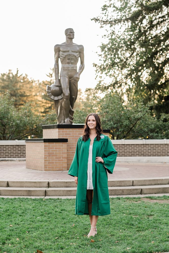 Michigan State graduation pictures on north campus in the fall with a white dress and grad gown with Sparty in the background by Allie & Co. Photography, East Lansing photographers