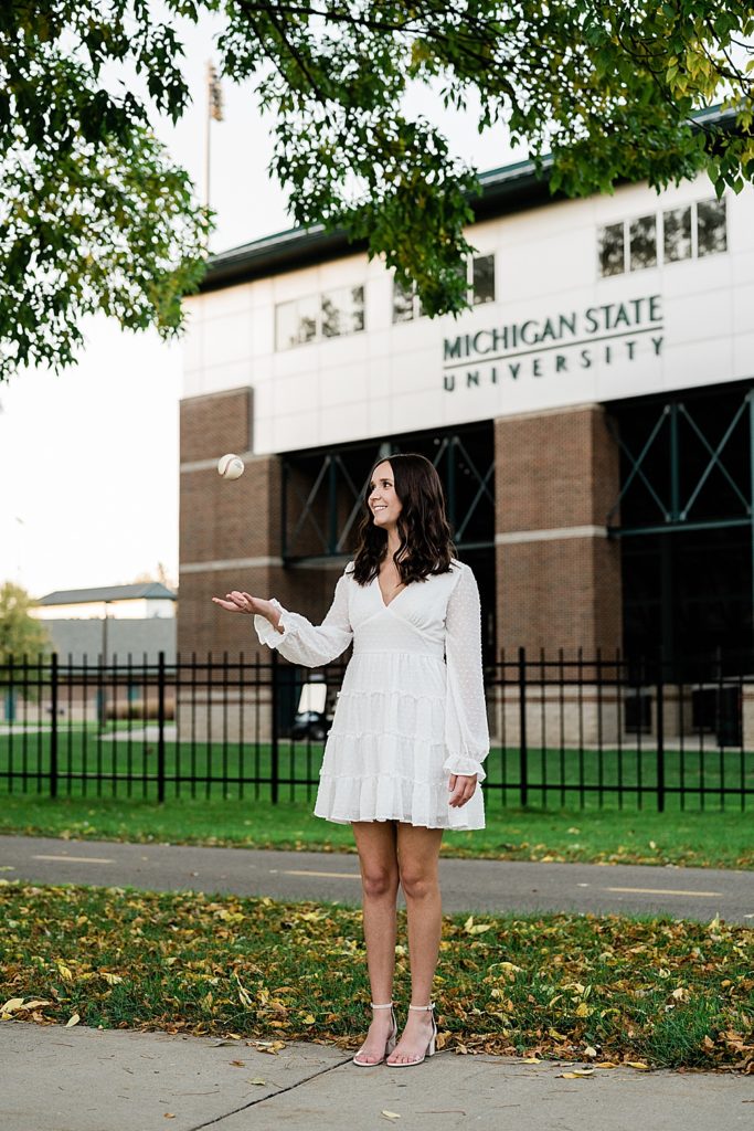 Michigan State graduation pictures on north campus in the fall with a white dress and McLane Baseball Stadium in the background by Allie & Co. Photography, East Lansing photographers
