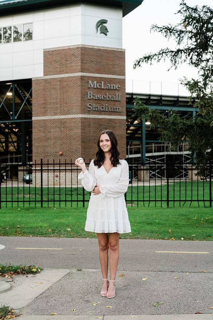 Michigan State graduation pictures on north campus in the fall with a white dress and McLane Baseball Stadium in the background by Allie & Co. Photography, East Lansing photographers