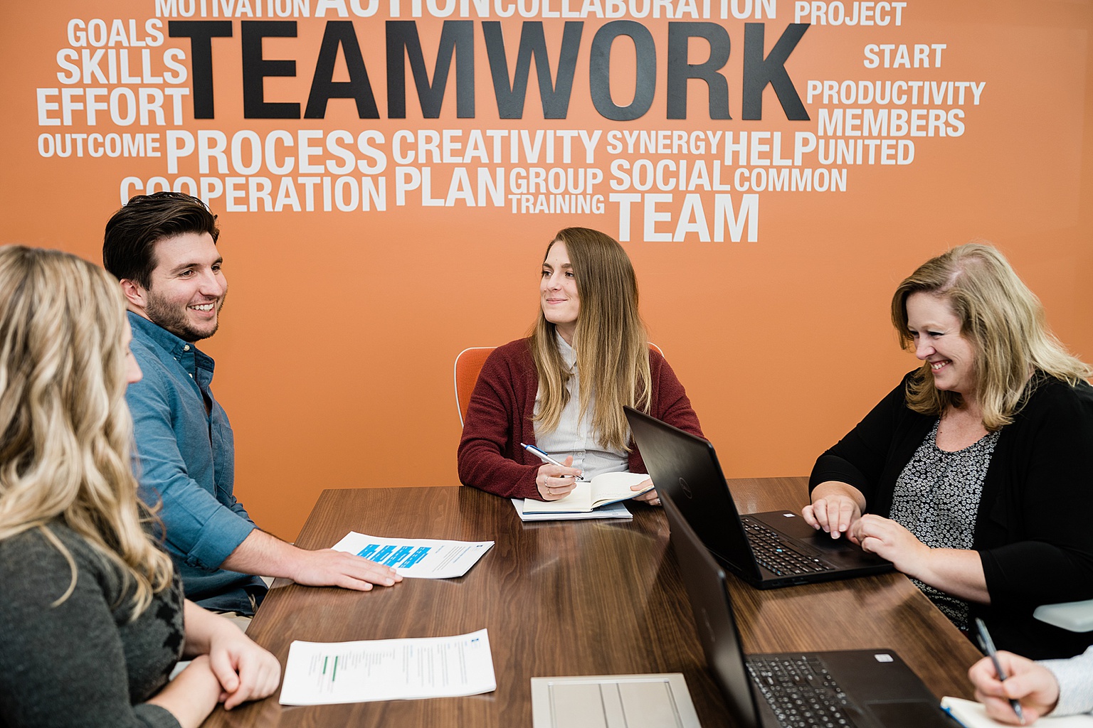 Lansing commercial photography - photos of team members around a table talking to each other with an orange wall behind them, by Allie Siarto & Co., Lansing branding and commercial photographer 