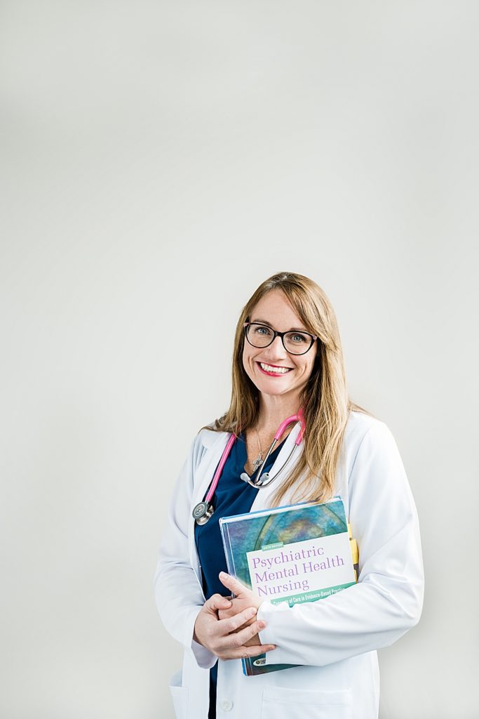 Lansing headshot photographer, photo of a nurse in her uniform holding a book against a white background, by Allie Siarto & Co, Lansing, Michigan branding photographers