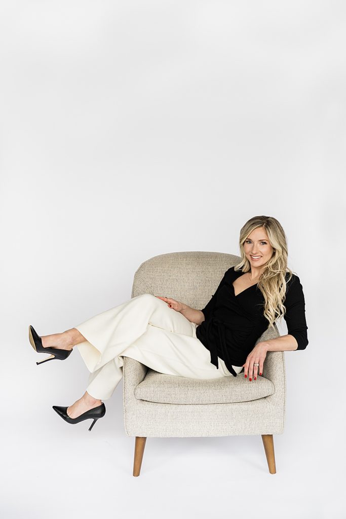 Lansing headshot photographer, photo of a woman sitting in a gray chair with her feet up in stilettos against a white seamless backdrop, by Allie Siarto & Co, Lansing, Michigan branding photographers