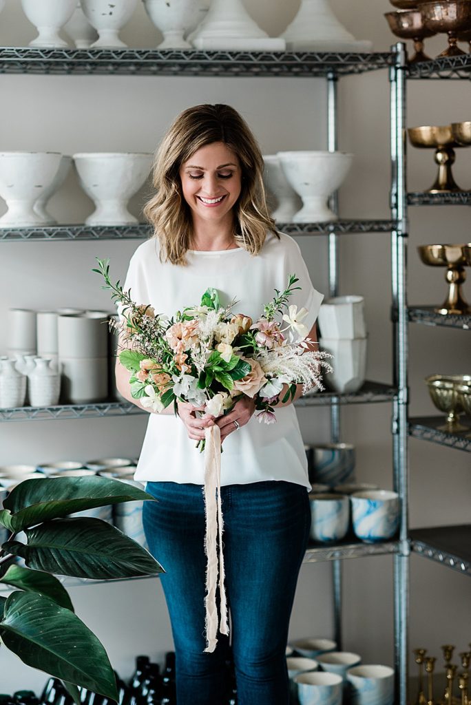 Lansing headshot photographer, photo of a florist holding a bouquet of flowers standing in her shop with shelves of vases behind her, by Allie Siarto & Co. Photography, Michigan branding photographers