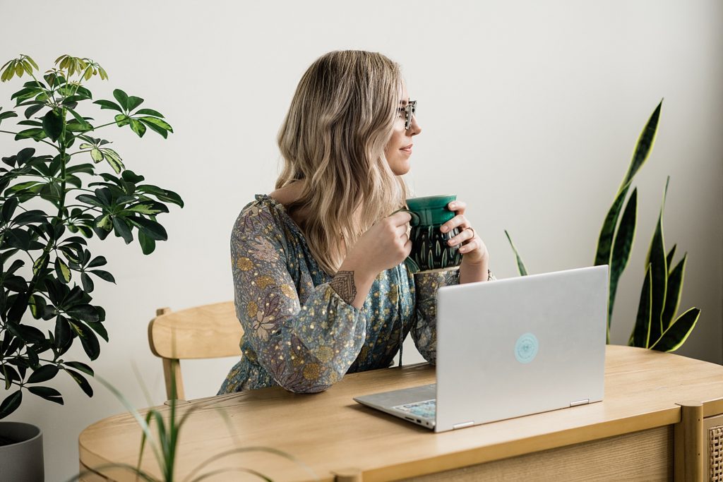 Lansing head shot photographer, photo of a woman looking to the side holding a mug of coffee while sitting at a desk with a laptop, by Allie Siarto & Co. Photography, Michigan branding photographers