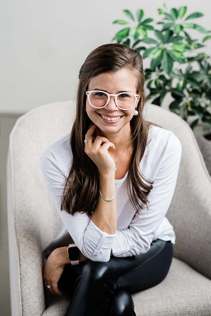 Lansing head shot photographer, photo of a woman in a white top and leather pants with white glasses smiling at the camera, by Allie Siarto & Co. Photography, Michigan branding photographers