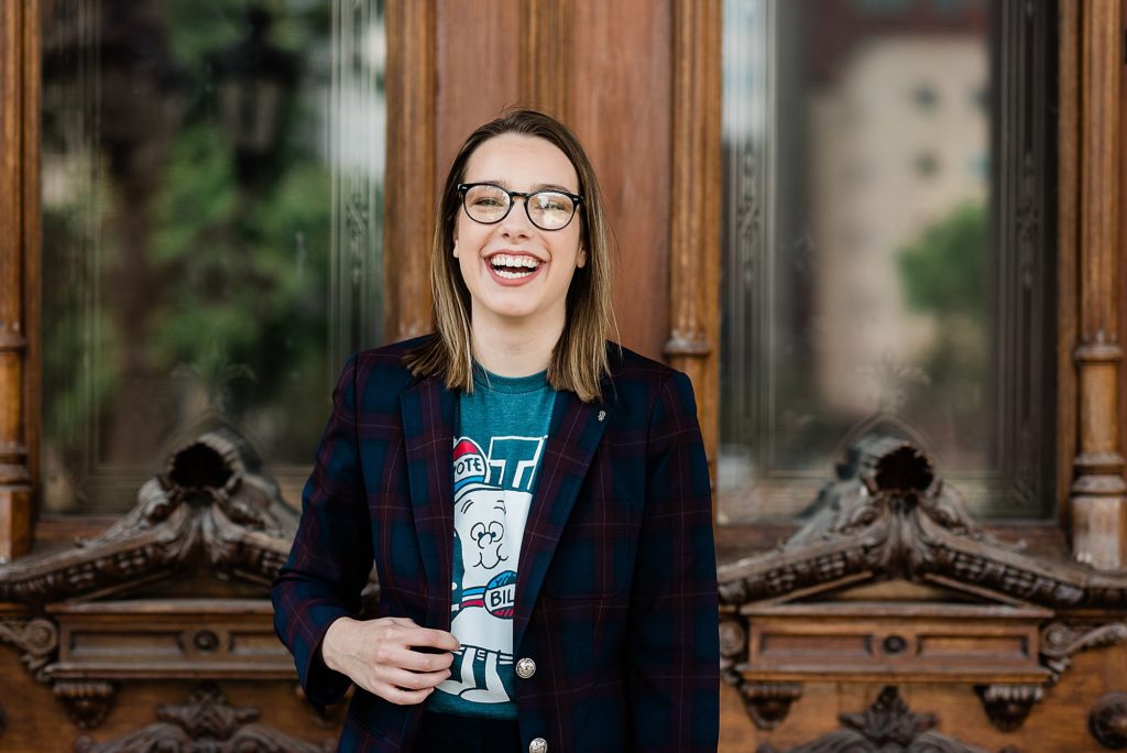 Lansing head shot photographer, photo of woman with a schoolhouse rock "Vote" shirt on laughing as she stands by the doors of the Capital Building in Lansing, by Allie Siarto & Co. Photography, Michigan branding photographers