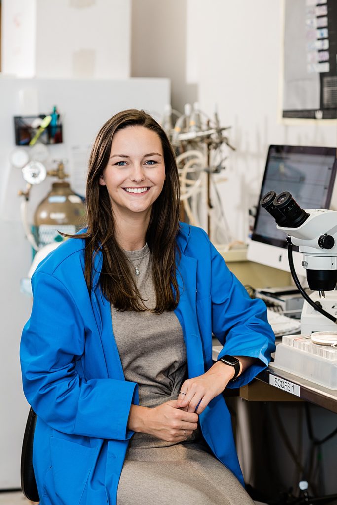 Lansing head shot photographer, close up photo of a scientist smiling at the camera and sitting next to a microscope, by Allie Siarto & Co. Photography, Michigan branding photographers