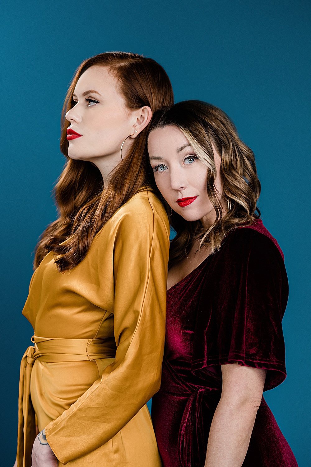 Lansing, Michigan commercial fashion photography, photo of two models - one in a yellow dress and one in a red velvet dress on a seamless blue backdrop by Allie Siarto & Co., Lansing commercial photographer
