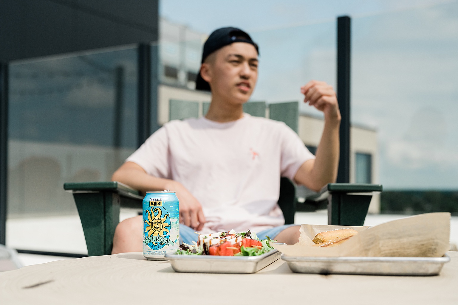 Graduate Rock bar commercial photography showing a student in the background with a can of Oberon and food in the foreground, by Allie Siarto & Co. Photography, Lansing, Michigan commercial photographers