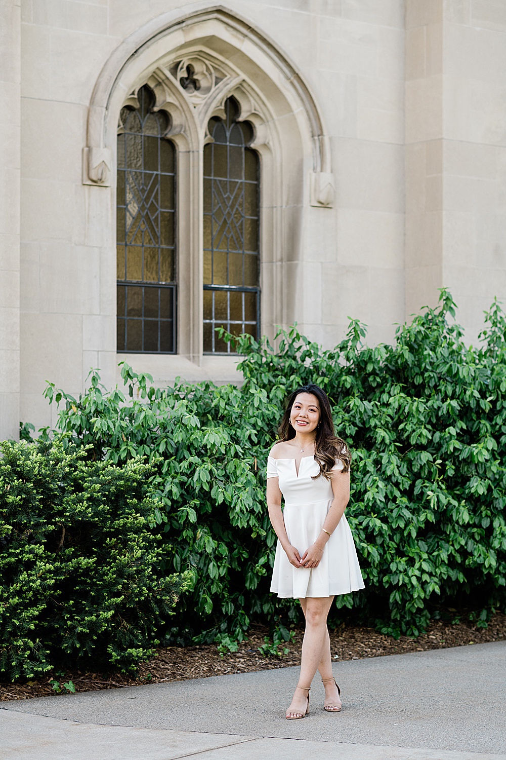 Michigan State Senior grad photoshoot on MSU's campus, photo of a woman in a white dress standing by a window on Beaumont Tower, by Allie Siarto & Co., East Lansing photographers