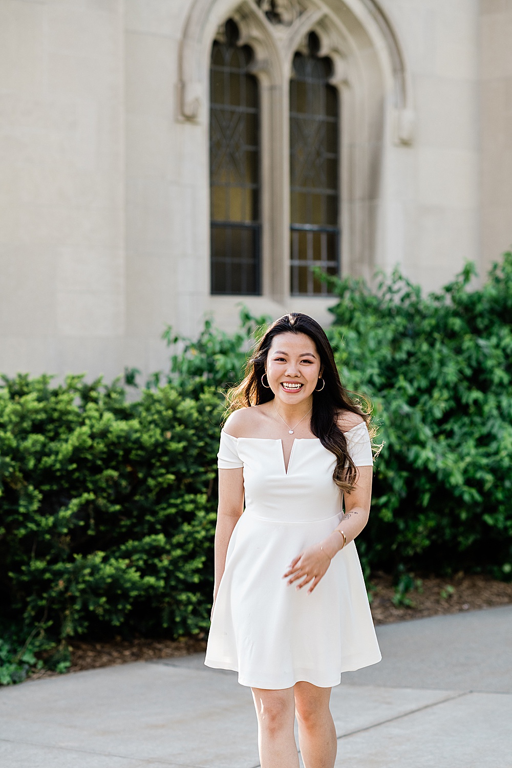 Michigan State Senior grad photoshoot on MSU's campus, photo of a woman in a white dress walking by a window on Beaumont Tower, by Allie Siarto & Co., East Lansing photographers