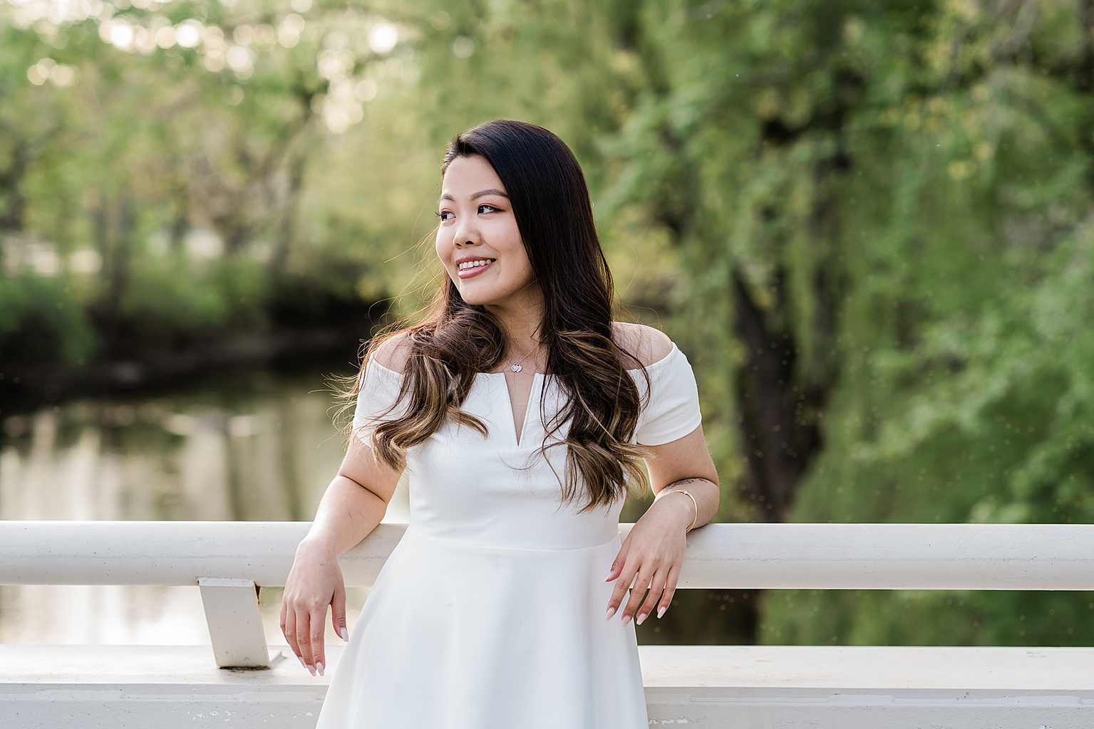 Michigan State Senior grad photoshoot on MSU's campus, photo of a woman in a white dress on the bridge by Spartan Stadium with the river in the background, by Allie Siarto & Co., East Lansing photographers