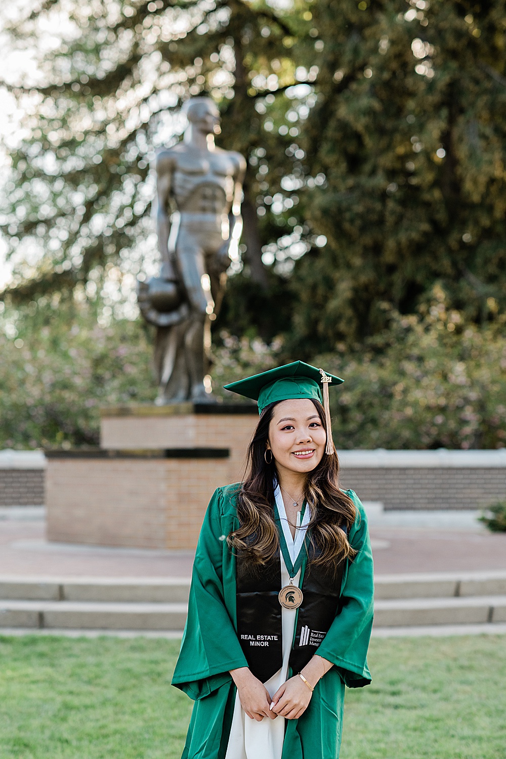 Michigan State Senior grad photoshoot on MSU's campus, photo of a woman in cap and gown in front of the Sparty statue, by Allie Siarto & Co., East Lansing photographers