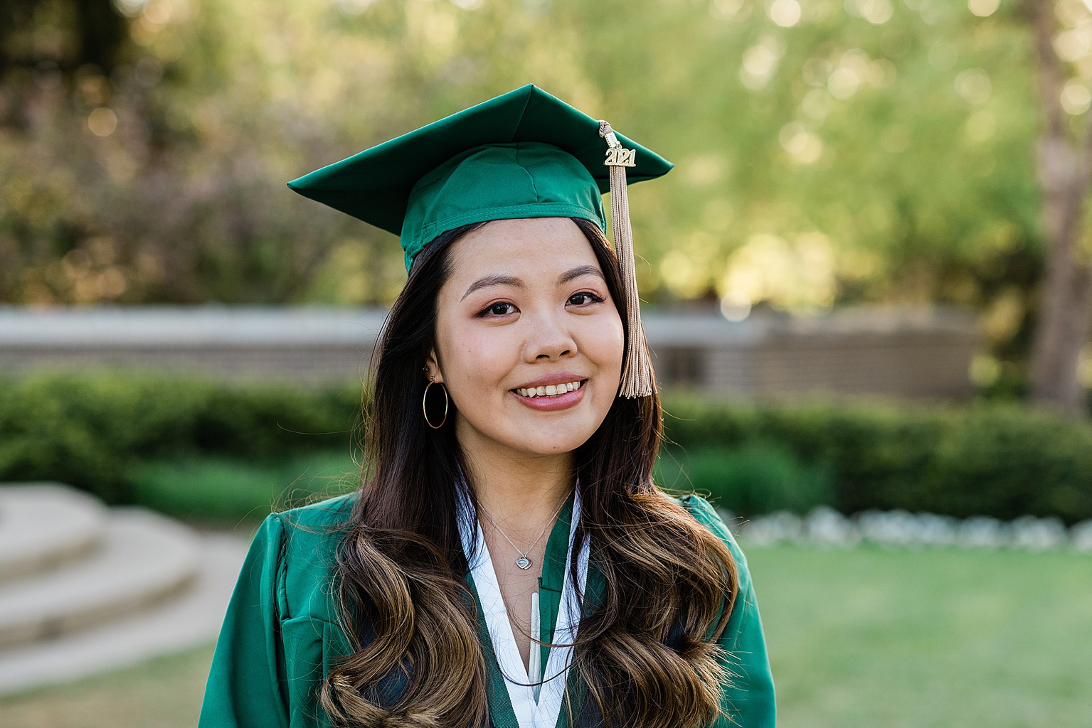 Michigan State Senior grad photoshoot on MSU's campus, photo of a woman wearing her cap and gown with golden hour light behind her, by Allie Siarto & Co., East Lansing photographers