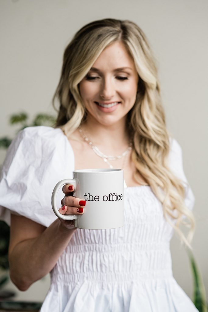 nurse injector branding photography, smiling at a coffee mug that says "The Office," by Allie Siarto & Co., Michigan headshot and branding photographers