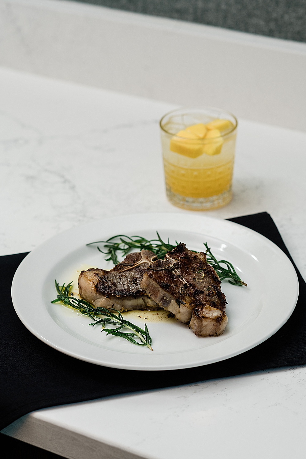 East Lansing's Graduate Hotel School Spirits Dinner, photo pork chops on a white plate with a yellow mixed drink, by Allie Siarto & Co. Photography, Lansing commercial photographer