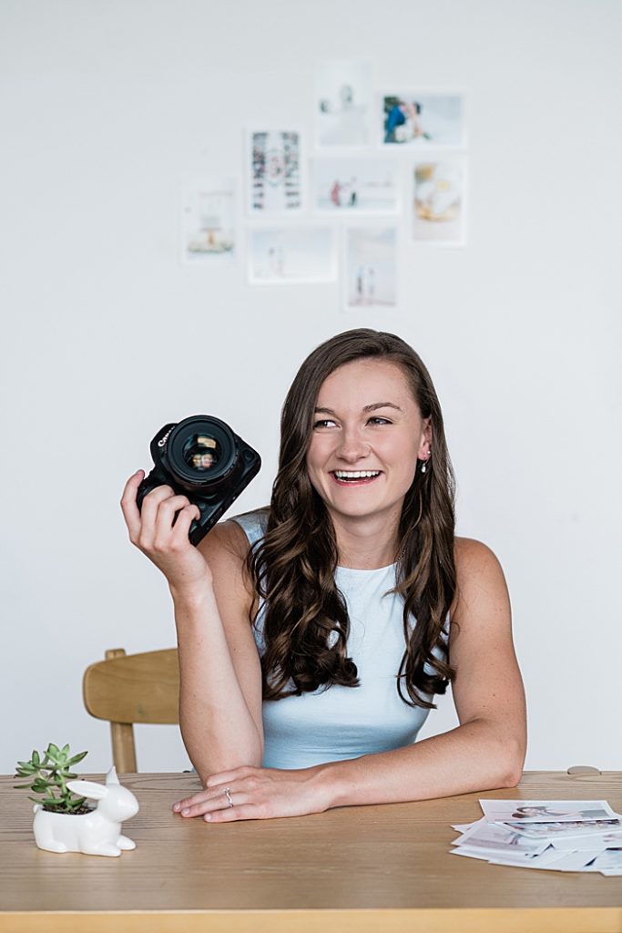 Lansing, Michigan headshot branding photos of a young photographer sitting at a desk holding a camera and smiling