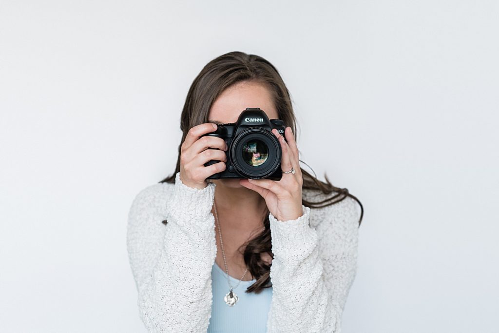 Lansing, Michigan headshot branding photos of a young photographer against a white backdrop holding her camera up to her face