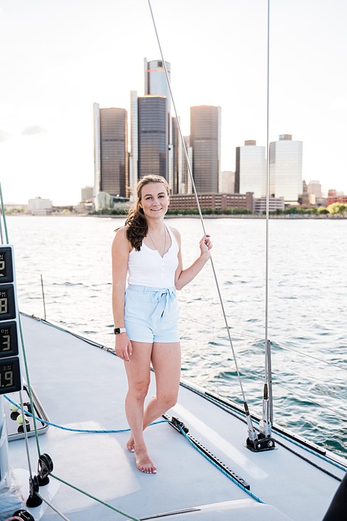 Detroit, Michigan headshot branding photos of a young photographer standing on a sailboat and smiling at the camera, surrounded by the Detroit River with the skyline of Detroit in the background - by Allie Siarto & Co. Photography, Michigan commercial and editorial photographers