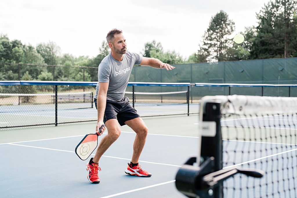 Product photo of a man wearing clothing from a pickle ball clothing line while playing pickle ball by Allie Siarto Photography, East Lansing, Michigan product photographers