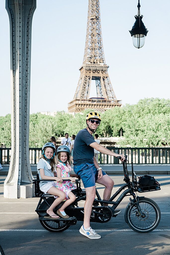 Riding a long tail cargo bike with kids in front of the Eifel tower in Paris, France.
