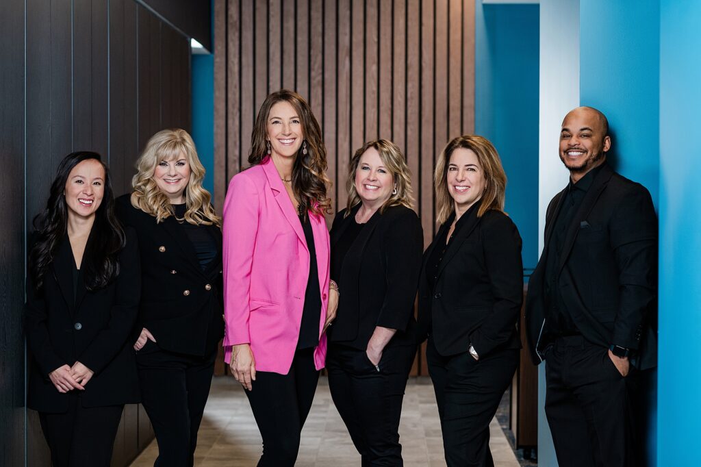 Marketing photos for a team of Lansing realtors, by Allie Siarto Photography, Lansing headshot and branding photographer; team photo of six realtors standing in a row with a wood background